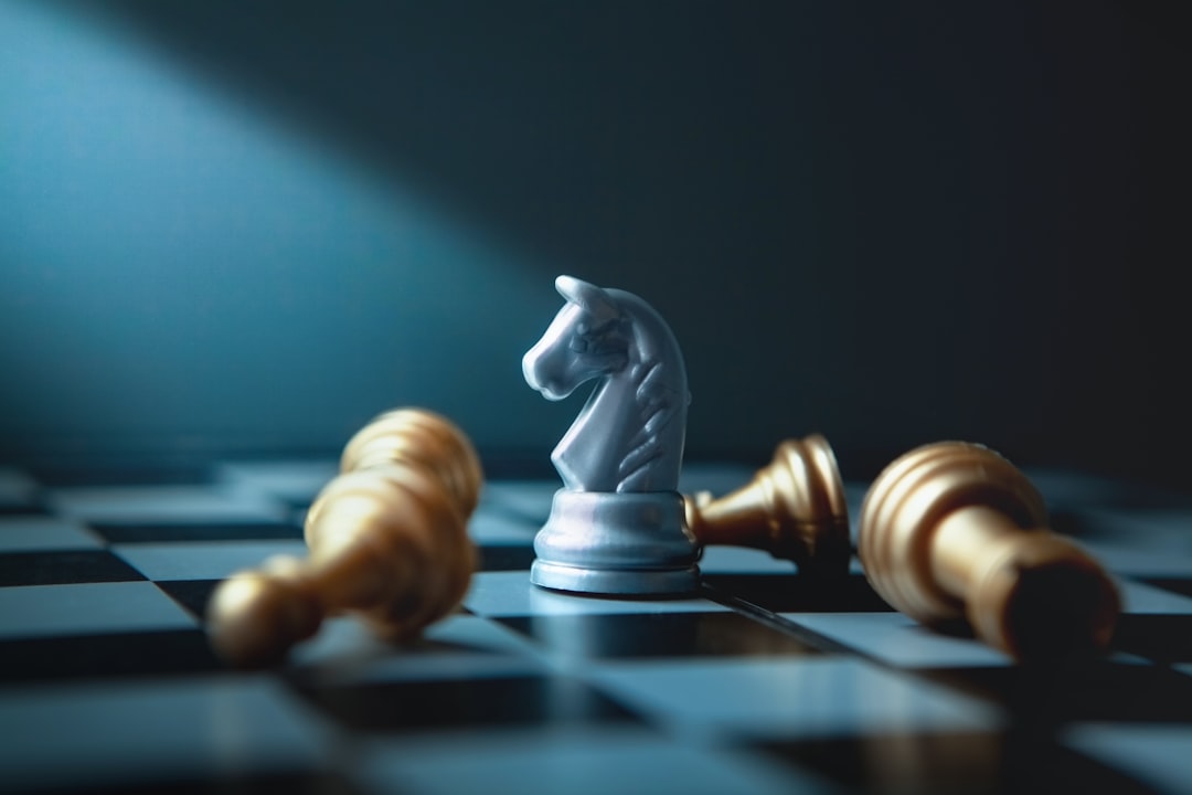 Silver knight chess piece standing among fallen golden pawns